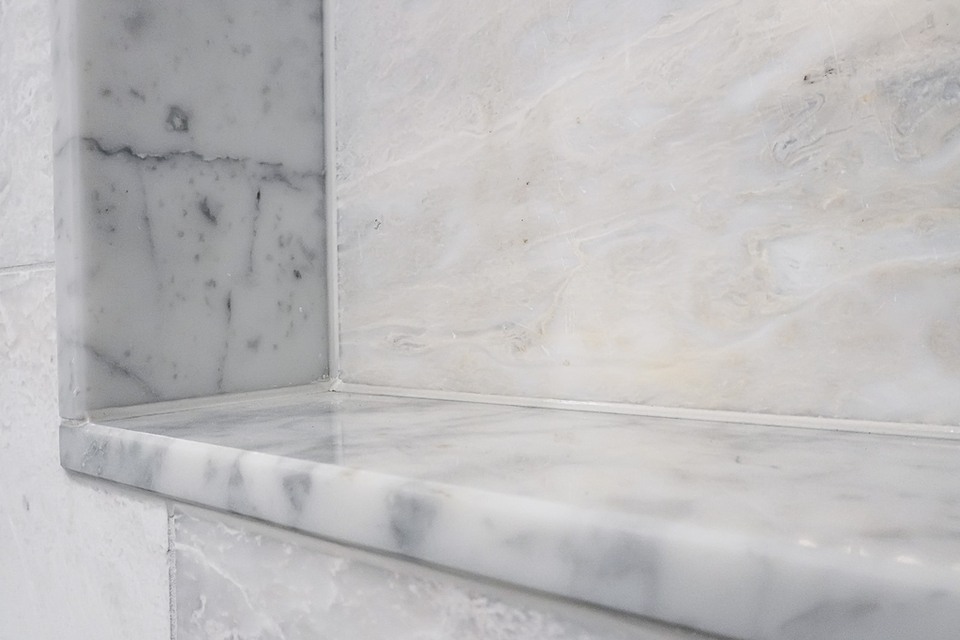 Close view of a recessed shower niche and marble-look sill projecting from the wall