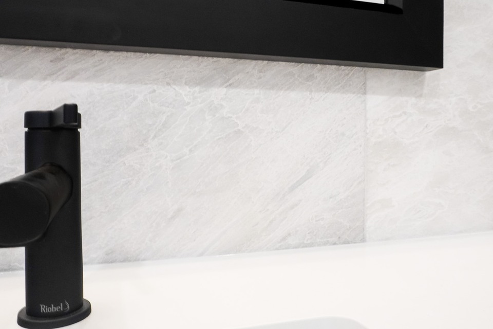 Black vanity tap and mirror against a white marble-look wall above a white sink