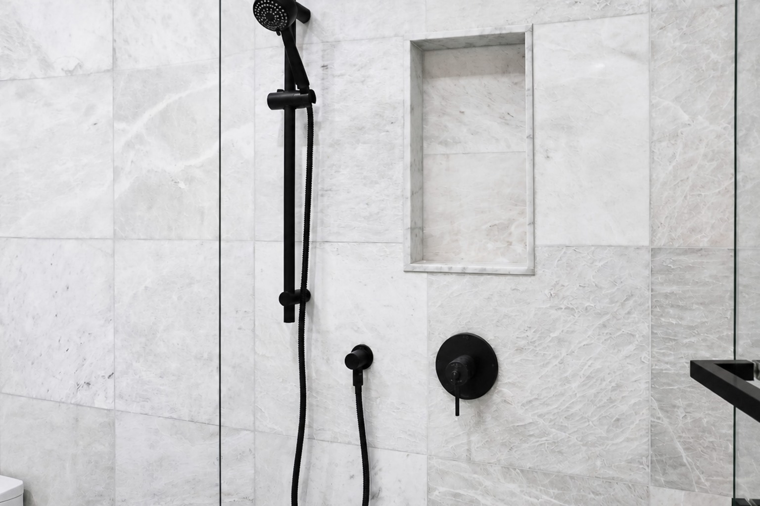White marble-look shower walls with a recessed niche, glass enclosure and black fittings