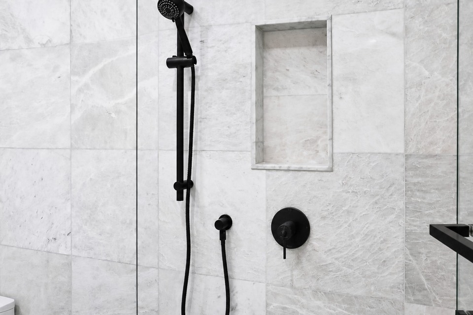 White marble-look shower walls with a recessed niche, glass enclosure and black fittings
