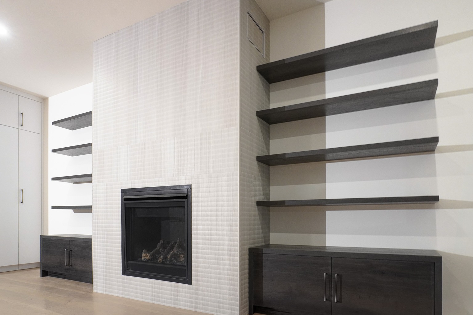 White textured fireplace surround between dark floating shelves and built-in cabinets
