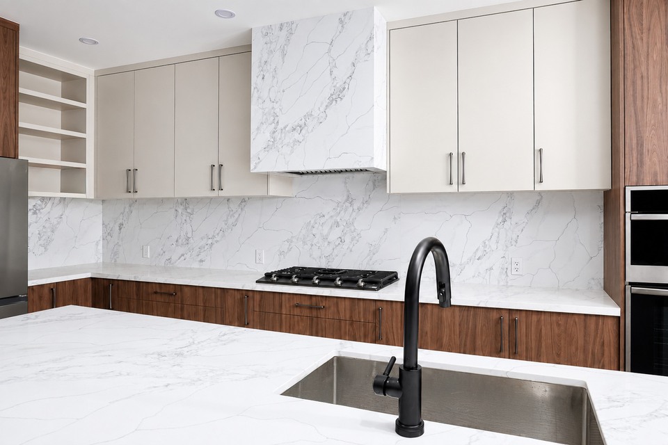 White marble-look kitchen backsplash and island beside white upper cabinets and wood lower cabinets