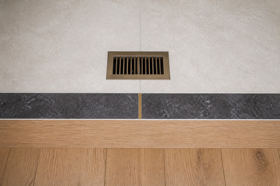 Detailed view of Scarborough porcelain floor tile cuts around the flush metal floor register and dark marble border