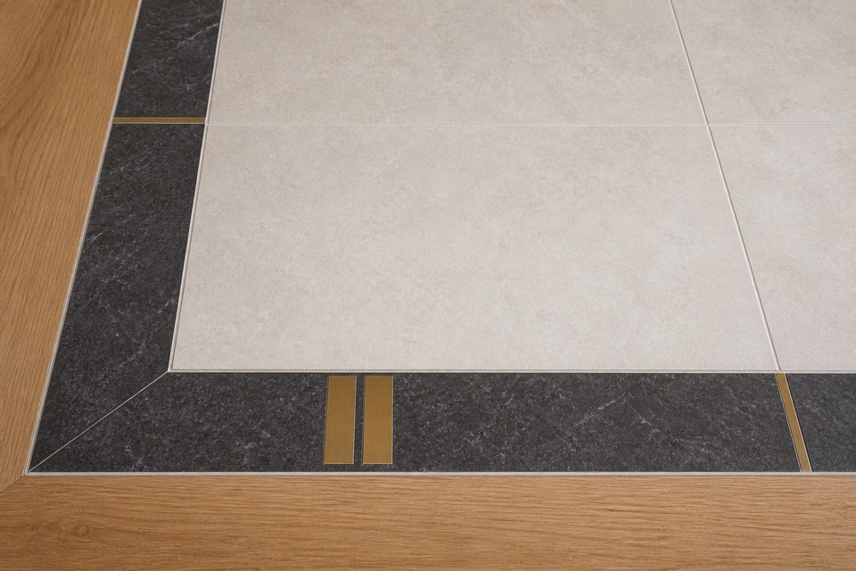 Close view of a dark floor border turning beside pale tile and oak