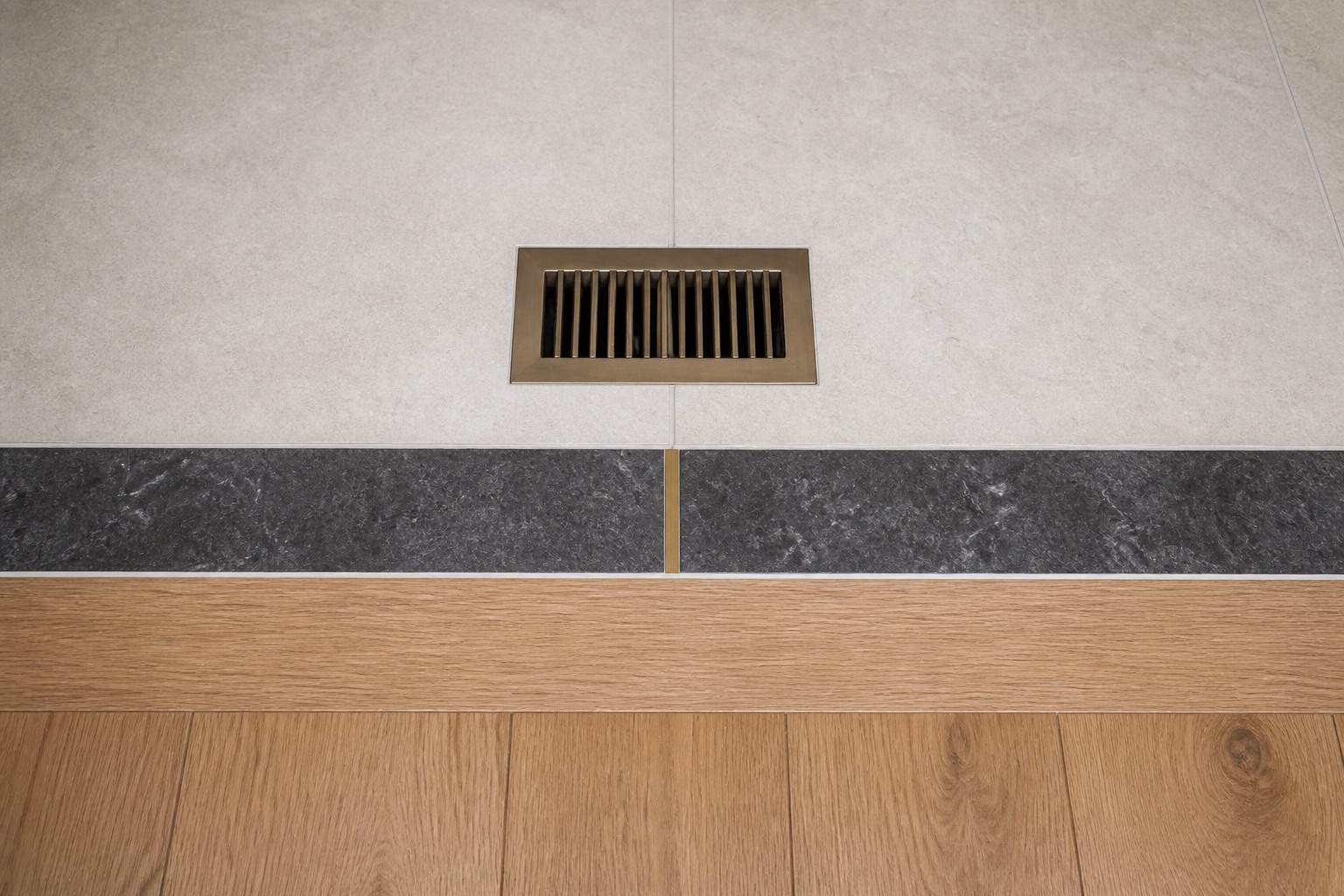 Close view of a floor register aligned with pale tile, a dark border and oak